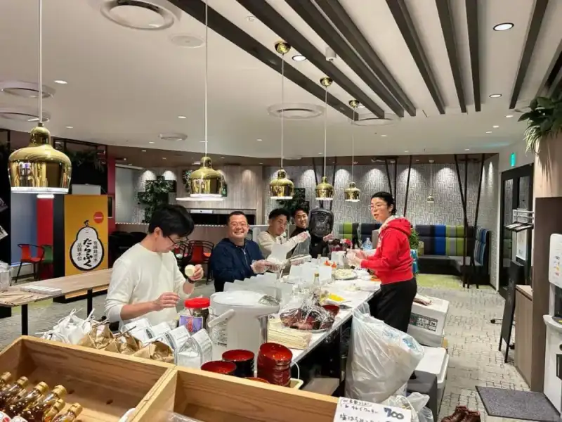 「たらふく」の看板の出店ブースで、保温ジャーと赤い椀、米袋を前に笑顔で準備する5人