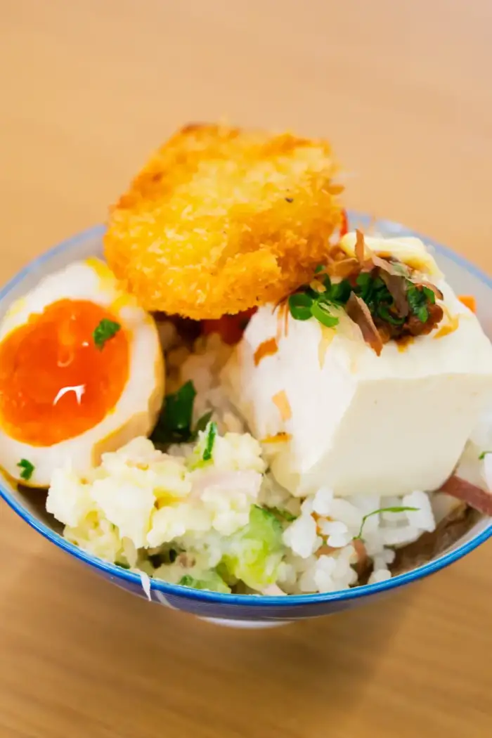 白いごはんの上に、揚げ物や卵、豆腐などのおかずを盛った丼