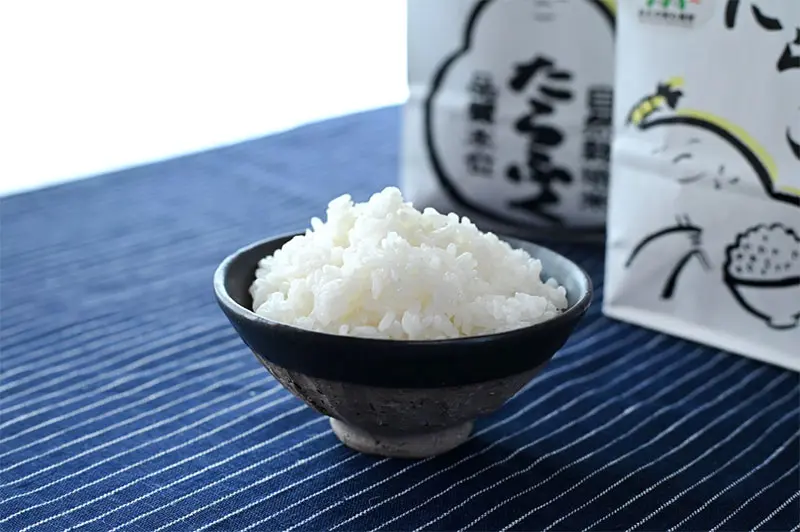 黒い茶碗に盛った白いごはんと、つじ農園の米袋